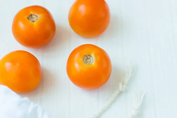 Top view of yellow cotton shopping bag with organic eco yellow tomatoes on white linen background.