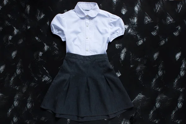 Camisa blanca, falda gris y artículos de papelería sobre fondo negro. El primero de septiembre, nuevo año escolar . — Foto de Stock