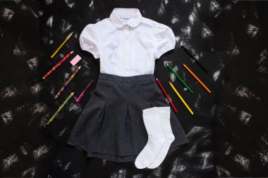 Beyaz gömlek, gri etek ve siyah arka plan üzerinde kırtasiye malzemeleri. Eylül'ün ilk, yeni öğretim yılı.