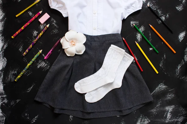 Camicia bianca, gonna grigia e cancelleria su sfondo nero. Il primo settembre, nuovo anno scolastico . — Foto Stock
