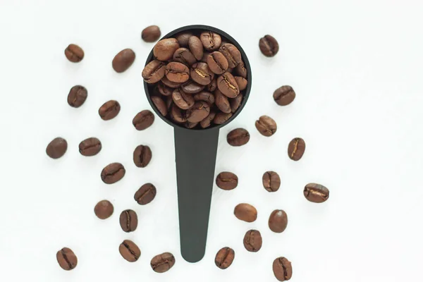 Braune geröstete Kaffeebohnen in einem schwarzen Messlöffel auf weißem Hintergrund isoliert. — Stockfoto