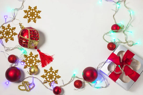 Рождественский подарок коробка с красной лентой, золотые украшения, шары, снежинки и огни на белом фоне . — стоковое фото