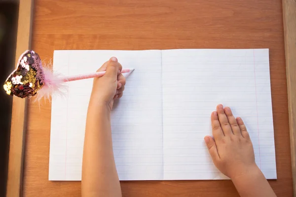 A child writes in an empty notebook on a wooden desk background. Back to school concept. Top view. — Stock Photo, Image