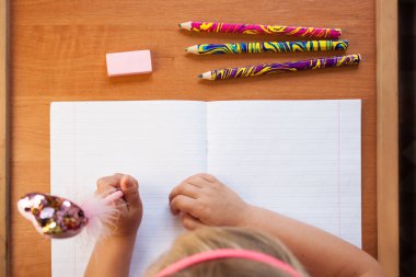 Bir çocuk ahşap masa arka planda boş bir not defterine yazar. Okul konseptine geri dönelim. Üst görünüm.