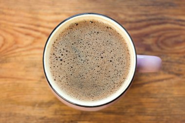 Ahşap arka planda bir fincan kahve. Güzel köpük, pembe seramik kupa, şık tonlama, kopya alanı.