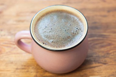 Ahşap arka planda bir fincan kahve. Güzel köpük, pembe seramik kupa, şık tonlama, kopya alanı.