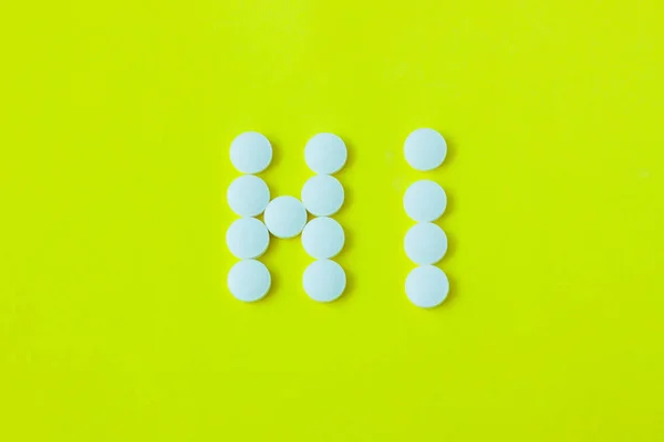 Pilulky ve tvaru slova Hi na žlutém pozadí. Plochá, vrcholní pohled, minimalistický styl. — Stock fotografie