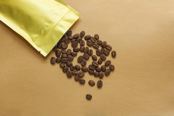 Gold foil bag with coffee beans on golden background. Packaging template mockup. Aluminium package for tea, flatlay.