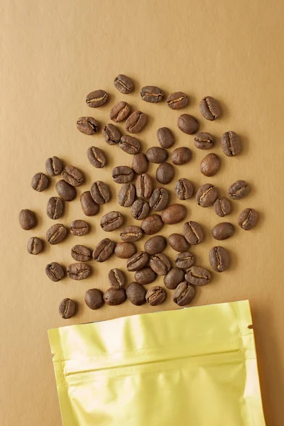 Gold foil bag with coffee beans on golden background. Packaging template mockup. Aluminium package for tea, flatlay.