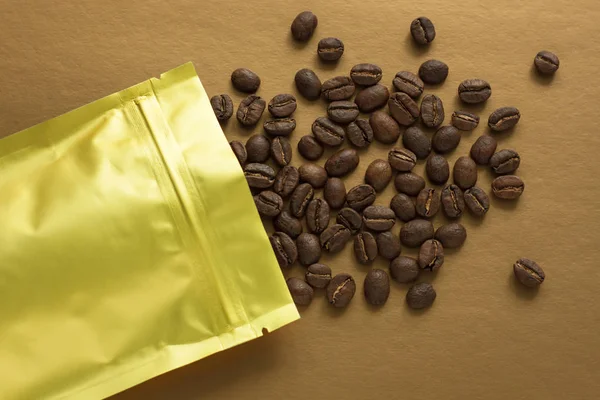 Gold foil bag with coffee beans on golden background. Packaging template mockup. Aluminium package for tea, flatlay.