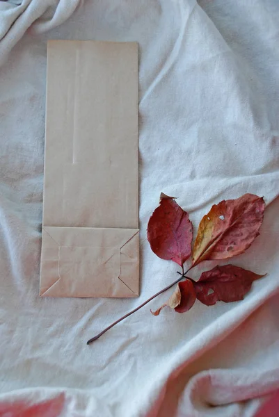 Kraft paper bags with autumn leaves on vintage linen fabric background.