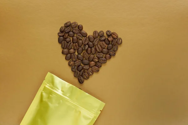 Gold foil bag with coffee beans on golden background. Packaging template mockup. Aluminium package for tea, flatlay.