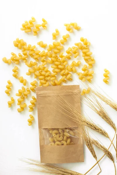 Pasta y espiguillas de trigo sobre un fondo blanco. Recetas de comida italiana. Vista superior, plano, espacio para copiar . — Foto de Stock