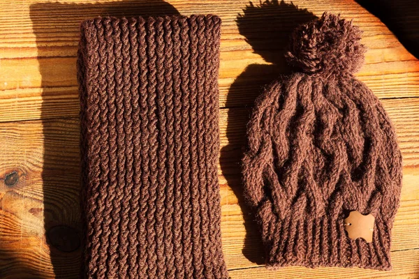 Sombrero y bufanda de punto marrón sobre fondo de madera con sombra de luz natural . — Foto de Stock