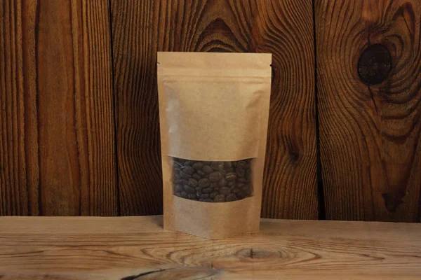 Brown kraft paper pouch bags with coffee beans front view on a wooden background.