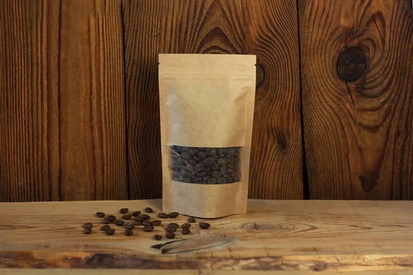 Sacos de bolsa de papel kraft marrom com vista frontal de grãos de café em um fundo de madeira . — Fotografia de Stock
