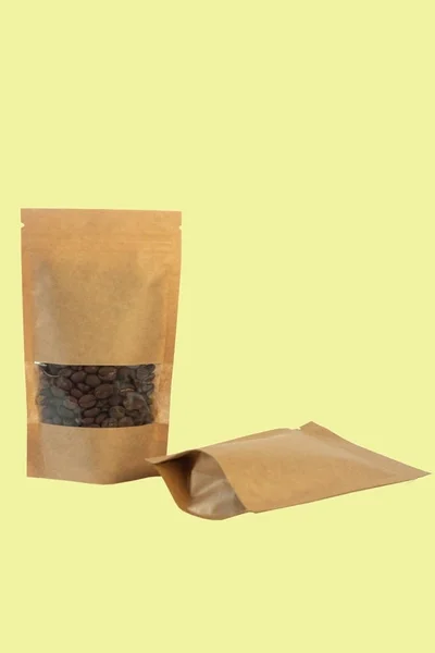 Бумажные мешки из крафта с кофейными зернами вид спереди на желтом фоне . — стоковое фото