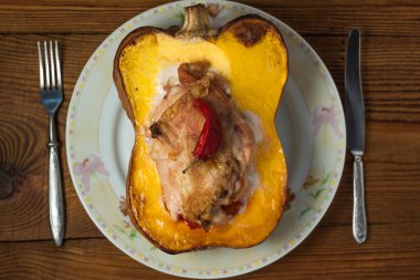 Balkabağı yarısı tavuk göğsü ve biberle doldurulmuş ahşap arka planda.