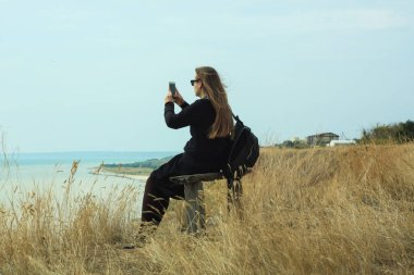Genç bir kadın akıllı telefonun ekranına bakar ve manzaranın fotoğrafını çeker..
