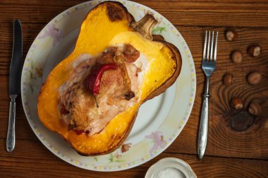 Balkabağı yarısı tavuk göğsü ve biberle doldurulmuş ahşap arka planda.