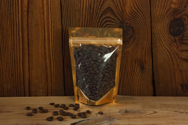 Brown kraft paper pouch bags with coffee beans front view on a wooden background.