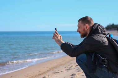 Mavi deniz manzaralı arka planda siyah yağmurluk giymiş sakallı bir adam. Elinde akıllı telefon ile konuşuyor. Orta yaşlı bir adam doğadan arkadaşlarını arıyor, insanlar yaşam tarzı konseptiyle iletişim kuruyor..
