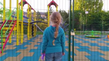 Karantina yüzünden kapalı oyun parkının yakınındaki üzgün yalnız çocuk. Uzun sarı saçlı bir kız çocuksuz, çitlerle çevrili boş bir alanda yalnız kalıyor. COVID-19 sosyal güvenlik mesafesi.