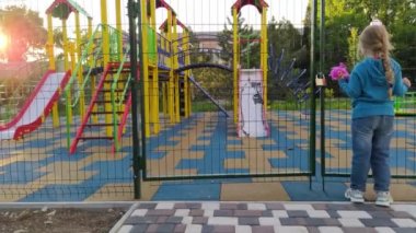 Karantina yüzünden kapalı oyun parkının yakınındaki üzgün yalnız çocuk. Uzun sarı saçlı bir kız çocuksuz, çitlerle çevrili boş bir alanda yalnız kalıyor. COVID-19 sosyal güvenlik mesafesi.
