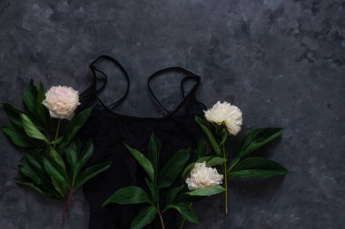 Kadınların göz kamaştırıcı siyah iç çamaşırları ve siyah arka planda beyaz şakayık çiçekleri olan mücevher aksesuarları. Kadın moda blog dairesi sosyal medya kopyalama alanı oluşturdu. Dantelli iç çamaşırı seksi gece kıyafetleri üst manzara.