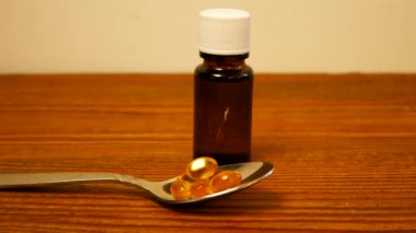 Çocuklar ve yetişkinler için D vitamini şişesi. D3 vitamini damlaları. Omega-3 takviyeli kapsüller masada duran kaşıkta saydam sarı toplar. Cam düşürücü şişe 4K Sağlık Hizmetleri