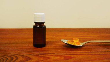Çocuklar ve yetişkinler için D vitamini şişesi. D3 vitamini damlaları. Masadaki kaşıkta saydam sarı toplar bulunan balık yağı Omega-3 takviyeli ilaçlar. Cam düşürücü şişe. Sağlık hizmetleri.