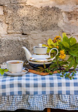 Kitap, sonbahar çiçekleri, yeşil üzüm dallı ahşap bankta çay fincanı. Sıcak bitkisel içecek. Beyaz porselen çay seti. Sıcak, taze havayla demlenmiş doğal içecekler. Sıcak sonbahar kahvaltısı.