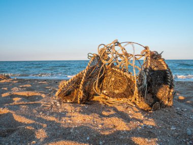 Eski, paslı telli kirli balık ağları, deniz kumsalındaki kumlara dökülen çöpler. Çevre kirliliği sorunu kavramı. Beş para etmez kumlu sahil. Mavi su arka planında dalgalar hareket ediyor. Gönüllü kavramı