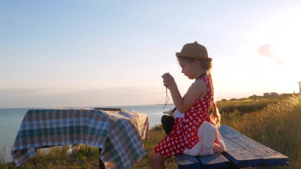 穿着草帽和衣服的小女孩坐在老式长椅上拍照 可爱的孩子 带着柔软的粉色兔子玩具 手里拿着笔记本 看着海景背景 友谊概念 — 图库视频影像
