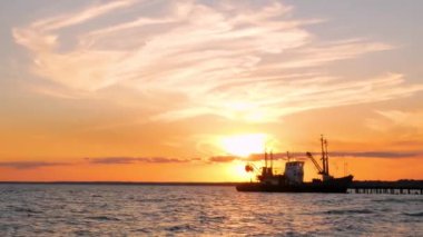 Deniz suyunda güzel turuncu gün batımı. Nakliye gemisi akşam limanda, deniz kıyısında. Deniz yoluyla nakliye lojistiği. Renkli bulutlu gökyüzü ile inanılmaz deniz manzarası.