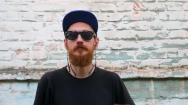 Siyah tişörtlü genç kızıl sakallı bir adamın portresi ve arka planda rock tarzında kulaklıkla müzik dinlerken. Kablosuz kulaklıklı hippi adam eski mavi tuğla duvar zemininde.