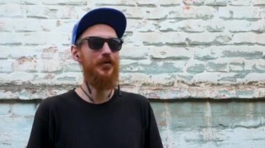 Siyah tişörtlü genç kızıl sakallı bir adamın portresi ve arka planda rock tarzında kulaklıkla müzik dinlerken. Kablosuz kulaklıklı hippi adam eski mavi tuğla duvar zemininde.