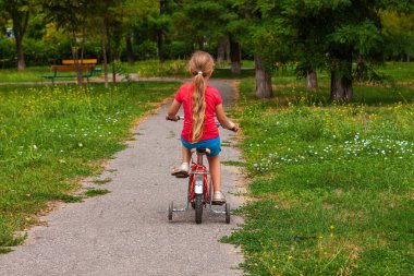 Çocuk bisiklete biniyor. Yazın asfalt yolda kırmızı bisikletli sarışın gülen kız. Aktif yaşam tarzı, spor stadyumunda fiziksel antrenman. Mutlu bir çocukluk. Çocuk bisikletçi..