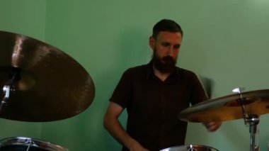 Davulcu davul fırçalarıyla ısınıyor. Sakallı adam yeşil duvar arkasında davulda rock ve metal müzik çalıyor. Müzik grubu provası 4K görüntü karıştırıyor.