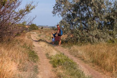 Bavullu baba ve kızı doğa manzarası üzerinde off-road yürüyorlar. Açık havada babasıyla kucaklaşan küçük sarışın kız. Sevgi dolu çocuk babasını kucaklıyor. Babalar Günü aile tebrik kartı..