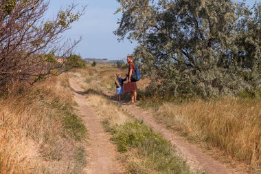 Bavullu baba ve kızı doğa manzarası üzerinde off-road yürüyorlar. Açık havada babasıyla kucaklaşan küçük sarışın kız. Sevgi dolu çocuk babasını kucaklıyor. Babalar Günü aile tebrik kartı..