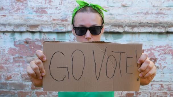 女孩展示硬纸板与去投票 在砖墙上签名城市背景 表决概念 做出政治选择 用你的声音 戴黑太阳镜的妇女呼吁去参加总统选举 — 图库视频影像