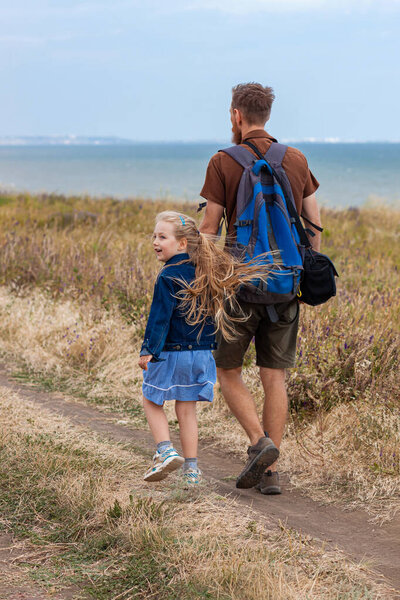 Отец с дочерью за руку стоят на холме с природой Лэнскейп. Маленькая блондинка обнимается с папой на открытом воздухе. Любящее дитя обнимает своего отца. Семейные открытки на День отца.