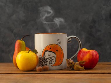 Kahve fincanlı yaratıcı Cadılar Bayramı kompozisyonu, arka planda meyveler ve fındıklar. Sonbahar tebrik kartı tasarımı, tatil kutlamaları sosyal medya şablonu. Elma, fındık, buharlı çay fincanı.