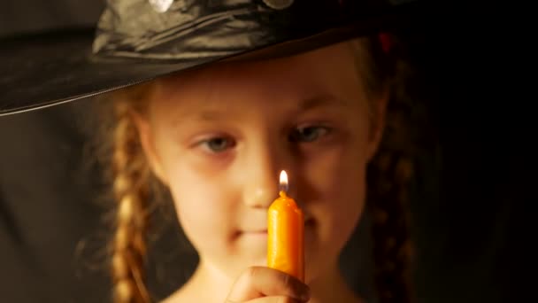 Маленькая Красивая Ведьма Шляпе Черного Волшебника Смотрит Горящую Свечу Дует — стоковое видео