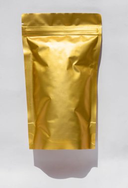 Üzerinde kahve çekirdekleri olan altın metalleştirilmiş çanta beyaz arka planda gölgelenmiş. Gıda ve mallar için ambalaj tasarımı. Çay yaprakları için tokalı paket, ağırlık ürünleri düz yatıyordu.