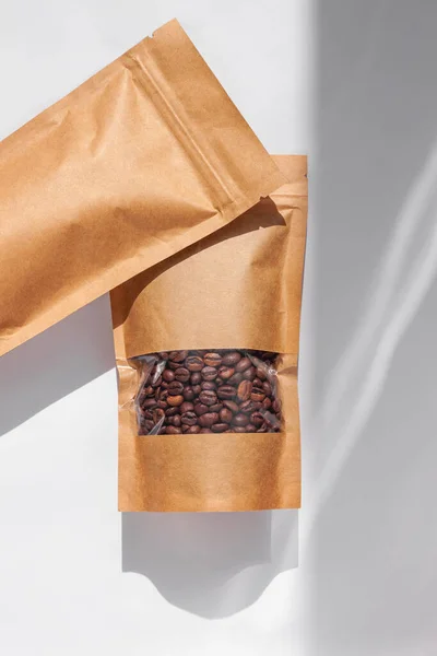 Brown kraft paper pouch bags with coffee beans top view with shadow isolated on white background. Packaging for foods and goods template mockup.Pack with clasp and window for tea leaves weight product