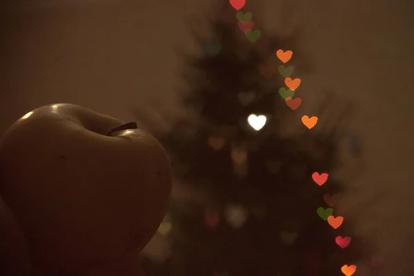 Green Apple on the background of the Christmas tree glowing neon lights garlands in the shape of hearts