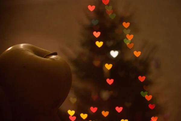 Green Apple on the background of the Christmas tree glowing neon lights garlands in the shape of hearts