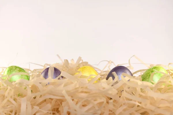 Cinque uova di colore pasquale in un nido di patatine lungo il fondo della cornice. Vista frontale . — Foto Stock